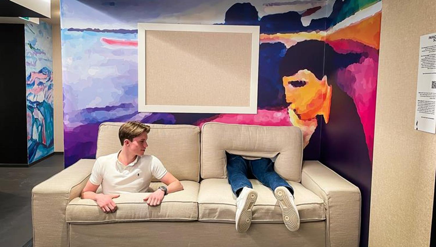 Beige sofa with a boy emerging from a hole, with a pair of legs appearing through a different hole next to him.