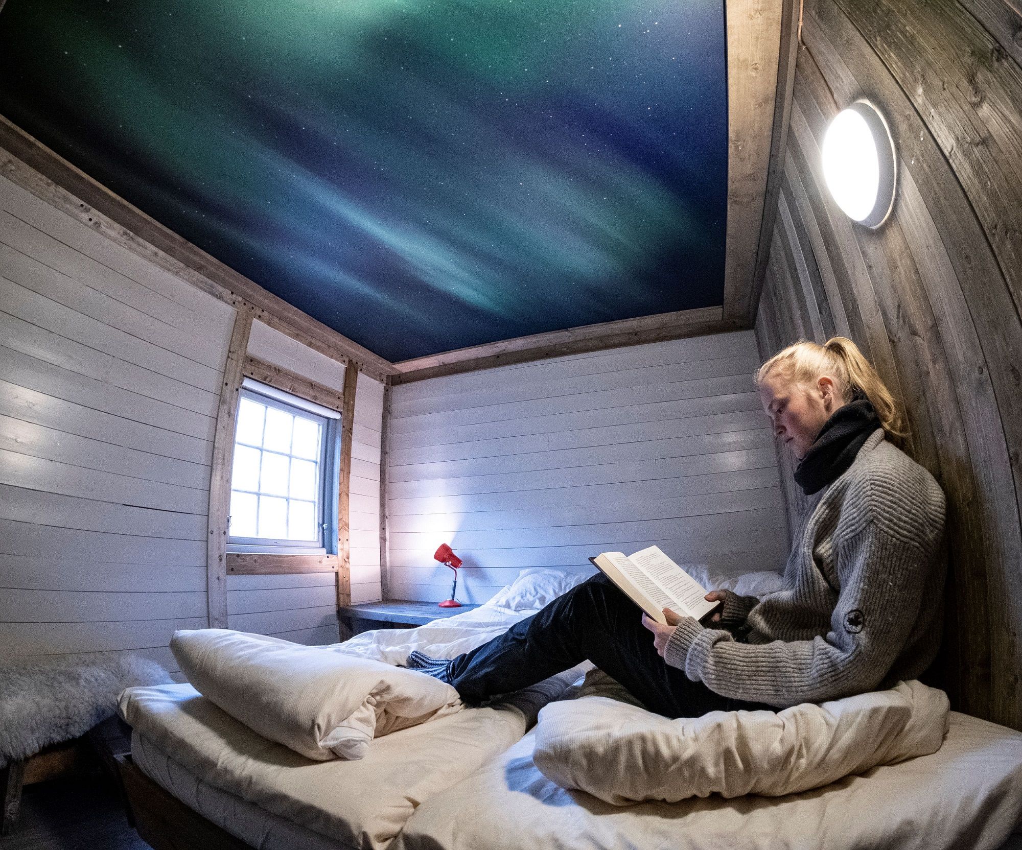 A guest sitting in a bed inside a bedroom reading a book