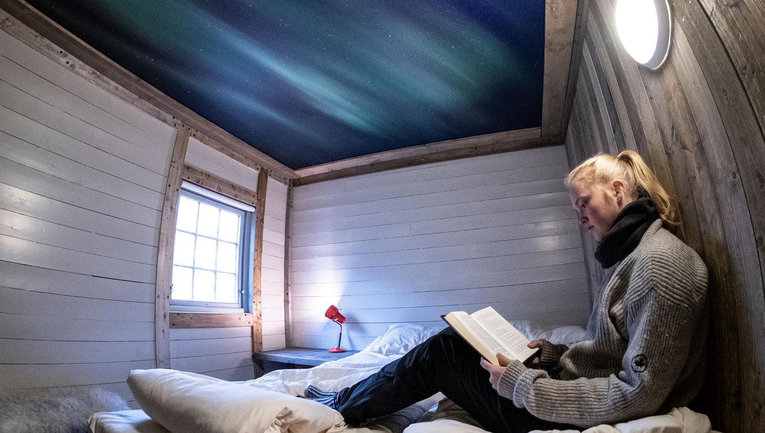 A guest sitting in a bed inside a bedroom reading a book