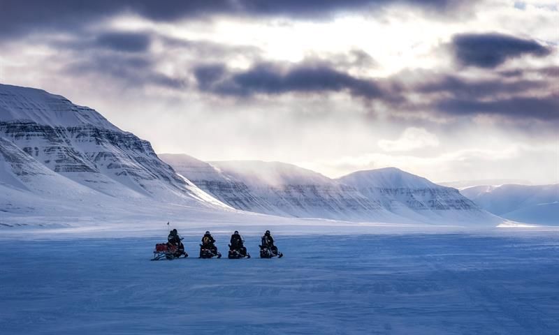 Snøscootere på vidde under dramatisk himmel.
