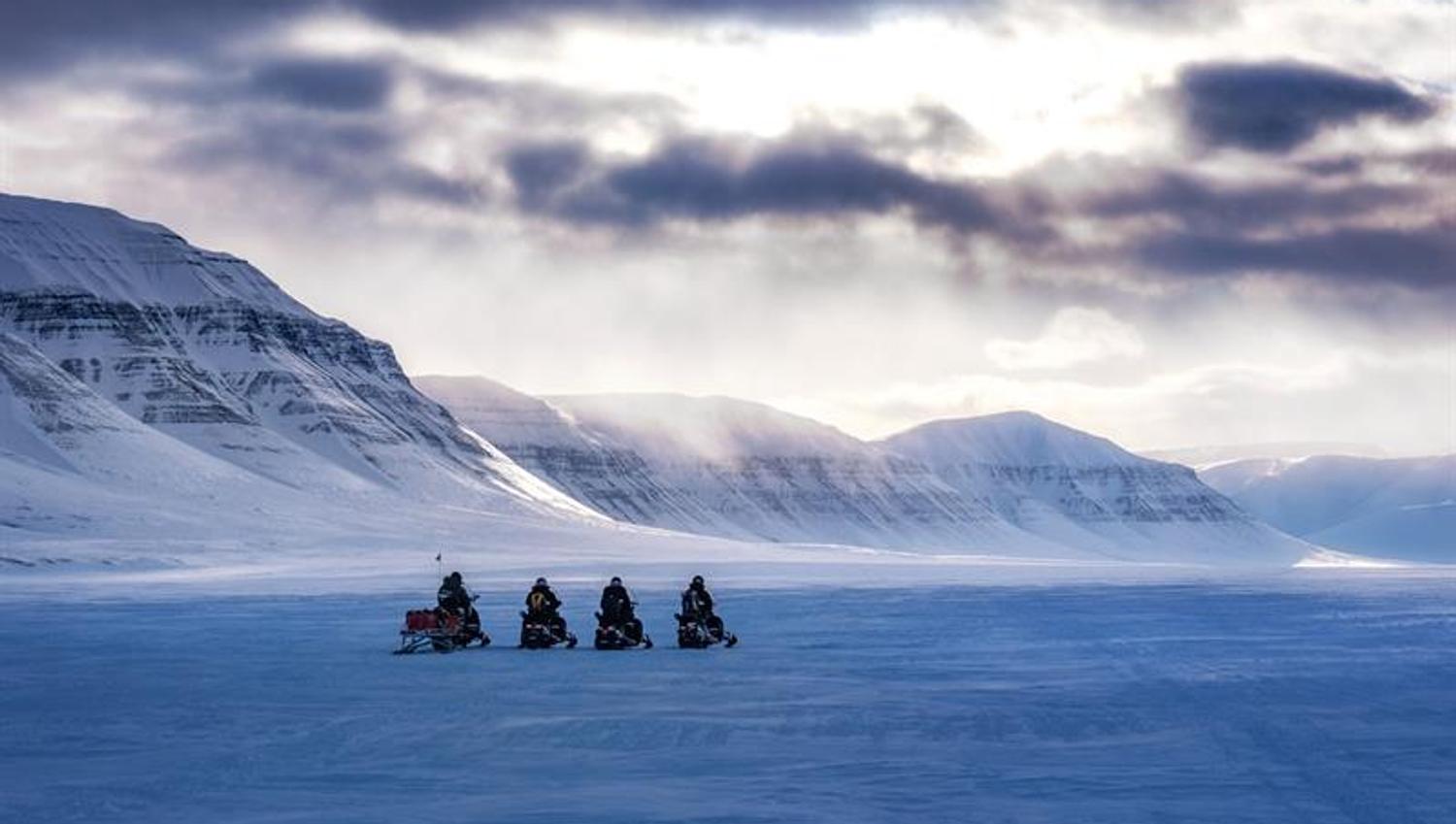 Snøscootere på vidde under dramatisk himmel.