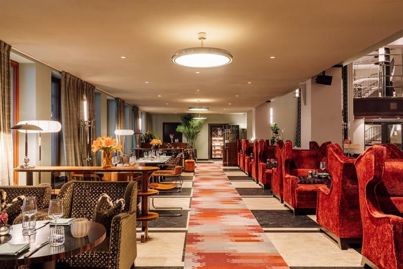 Elegant hotel lounge with comfortable armchairs, long tables, warm-coloured rugs, and an inviting atmosphere.