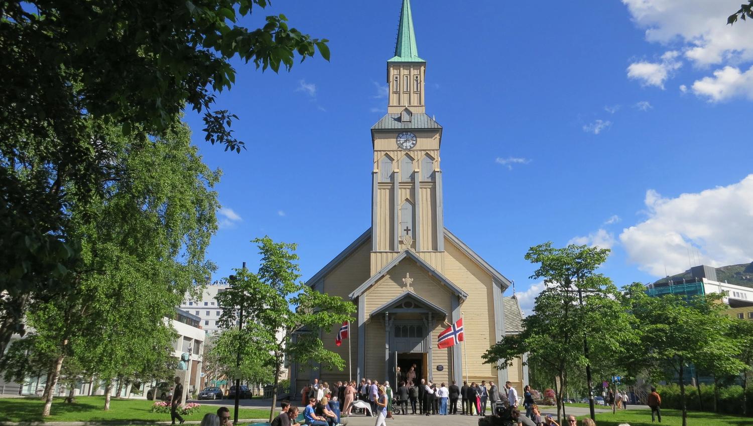 The cathedral with Norwegian flags, surrounded by people and trees on a sunny day.