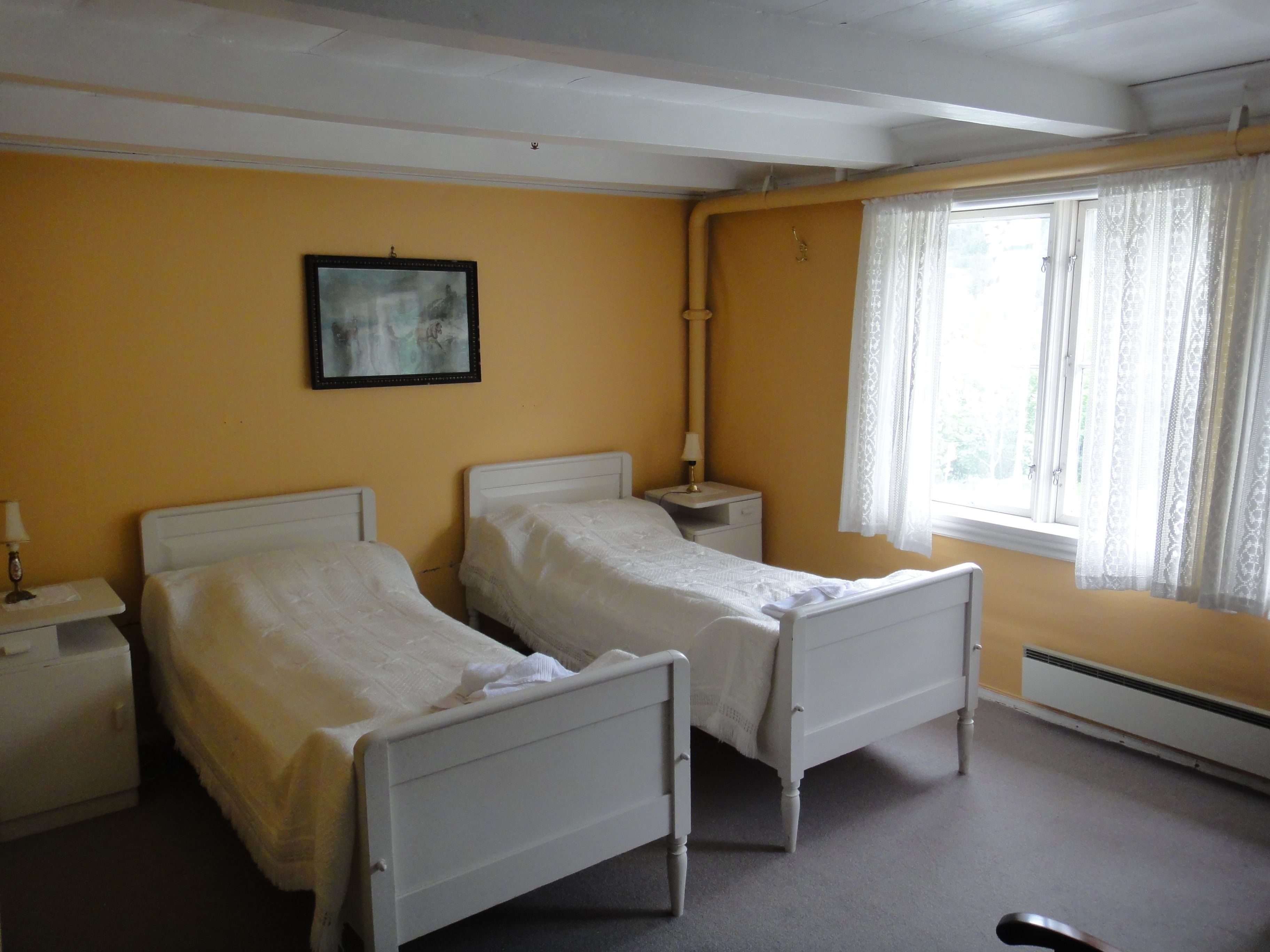 Traditional bedroom with two white beds and large windows at Jaunsen Guesthouse in Hardanger, Norway.