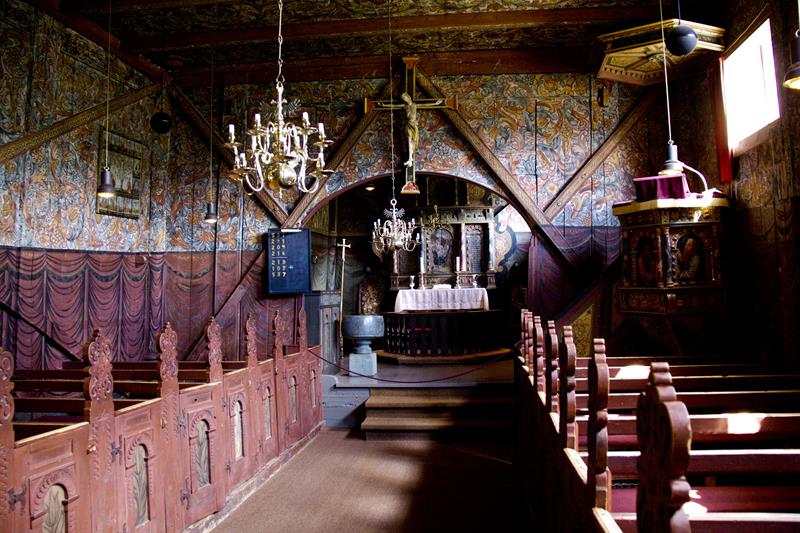 Richly painted interior of Røldal Stave Church featuring the altar, wood carvings, and medieval details.
