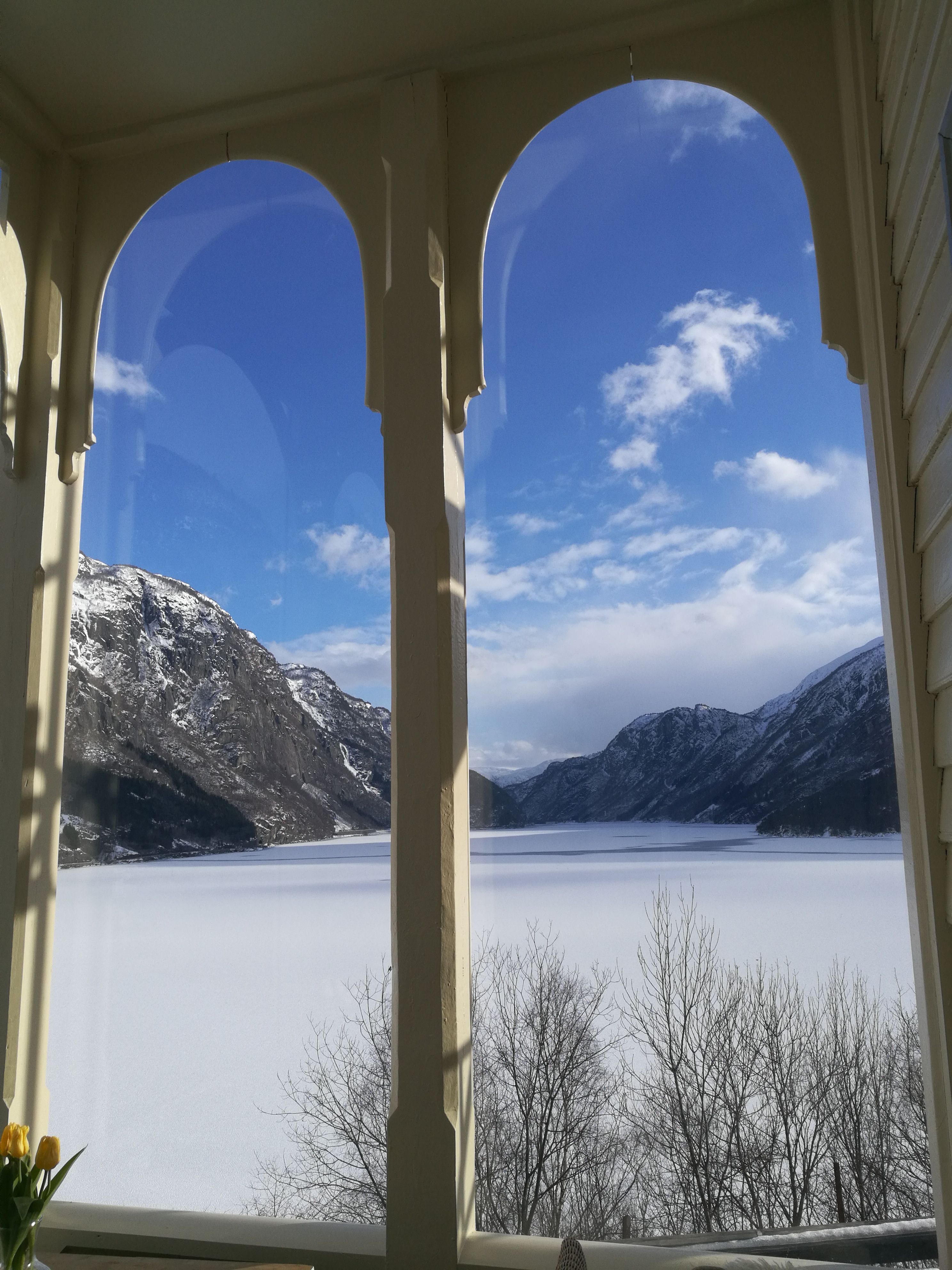 Stunning winter view from the veranda at Vikinghaug Apartments, overlooking snow-covered mountains and a calm fjord beneath a blue sky.
