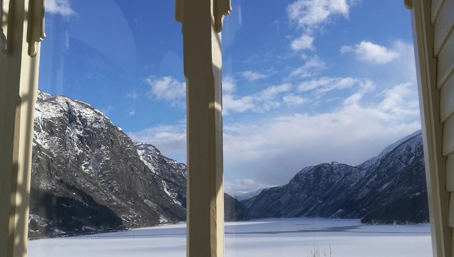 Stunning winter view from the veranda at Vikinghaug Apartments, overlooking snow-covered mountains and a calm fjord beneath a blue sky.