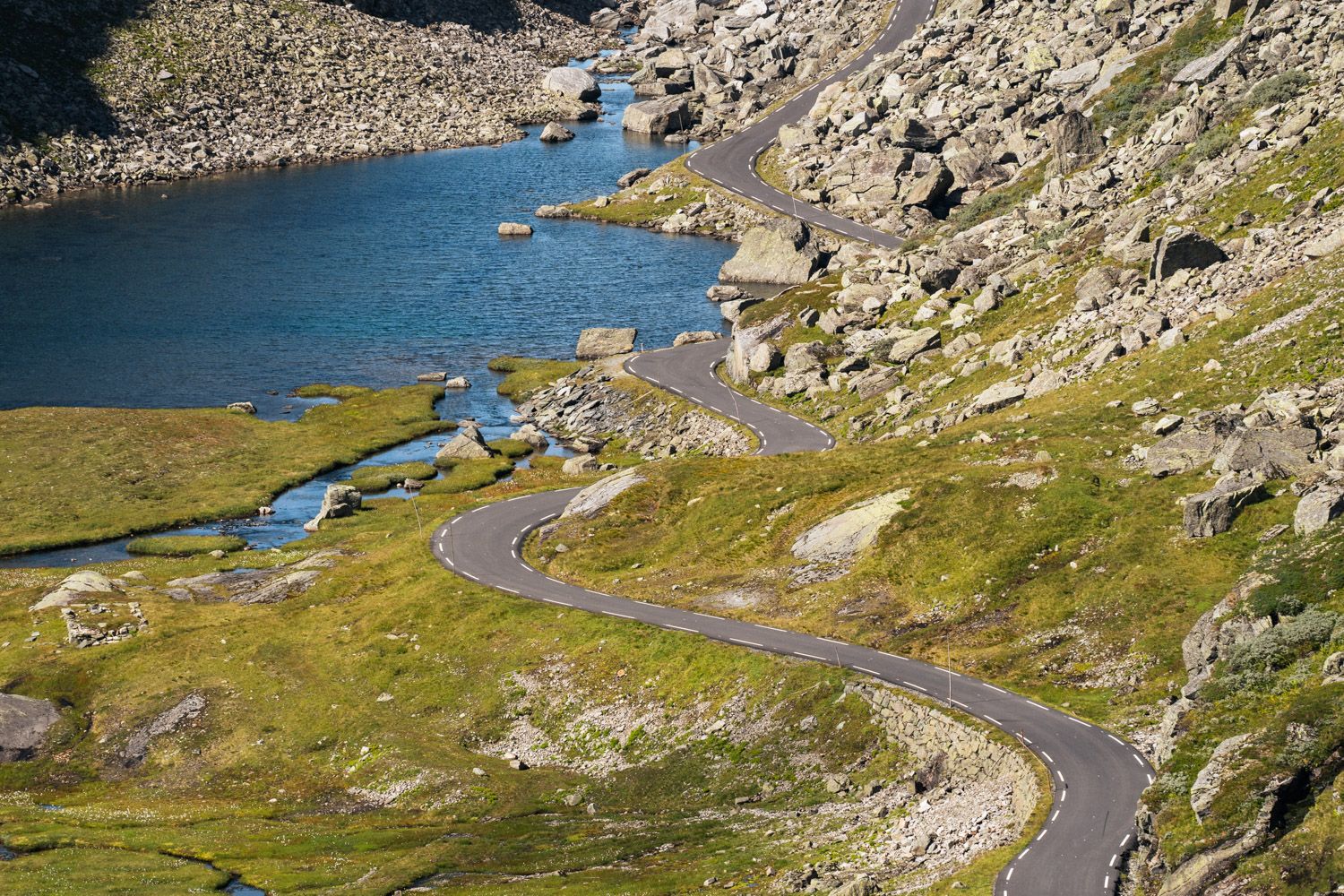 Grøntområder og bilveg som leder ned til eit vatn.