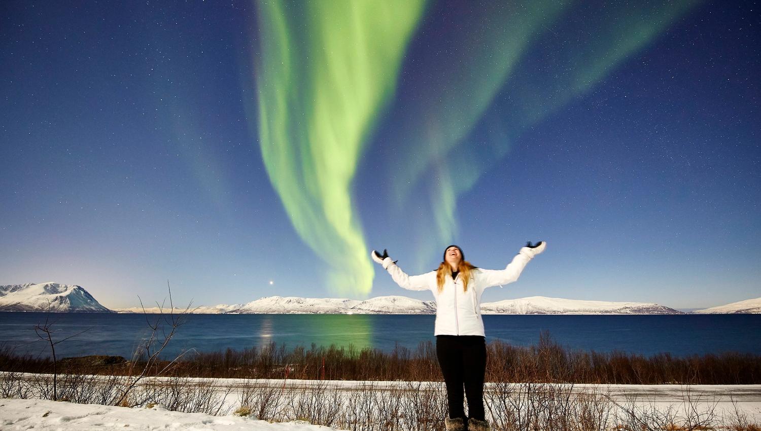 a woman standing with her arms up and looking at the sky where the northern lights are