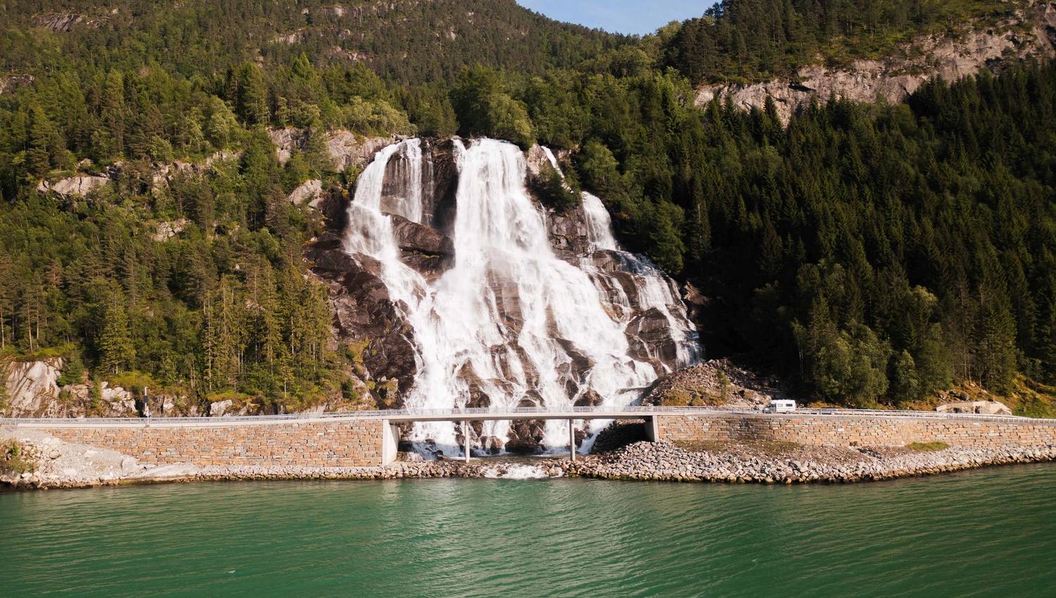 Furubergsfossen from the fjord – A majestic view of Furubergsfossen cascading down the cliffs beside the fjord in Kvinnherad, surrounded by lush green