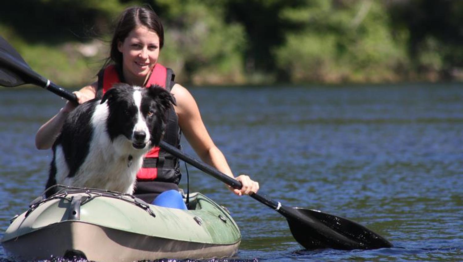 : A woman with a dog (border collie) in a green canoe paddling on the water