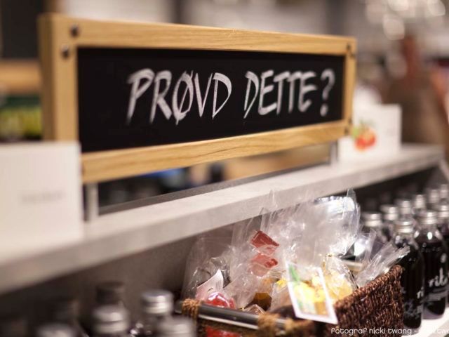 A sign reading “Tried this?” stands above a store shelf filled with bottles and packaged goods. The sign invites customers to try or buy something new