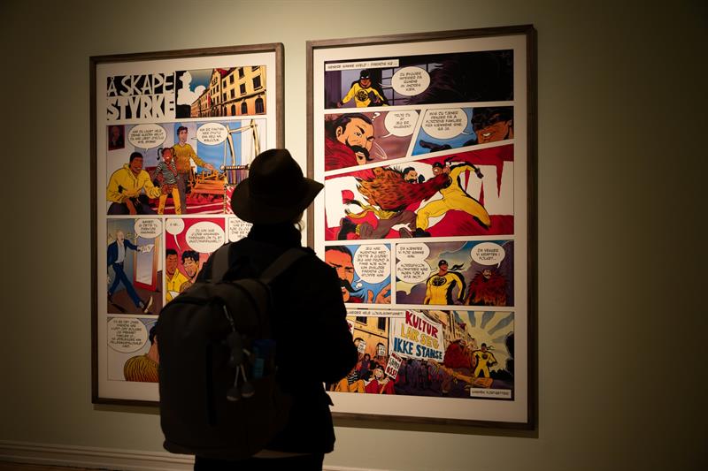 Visitor viewing framed comic book pages in a museum exhibition with subdued lighting.