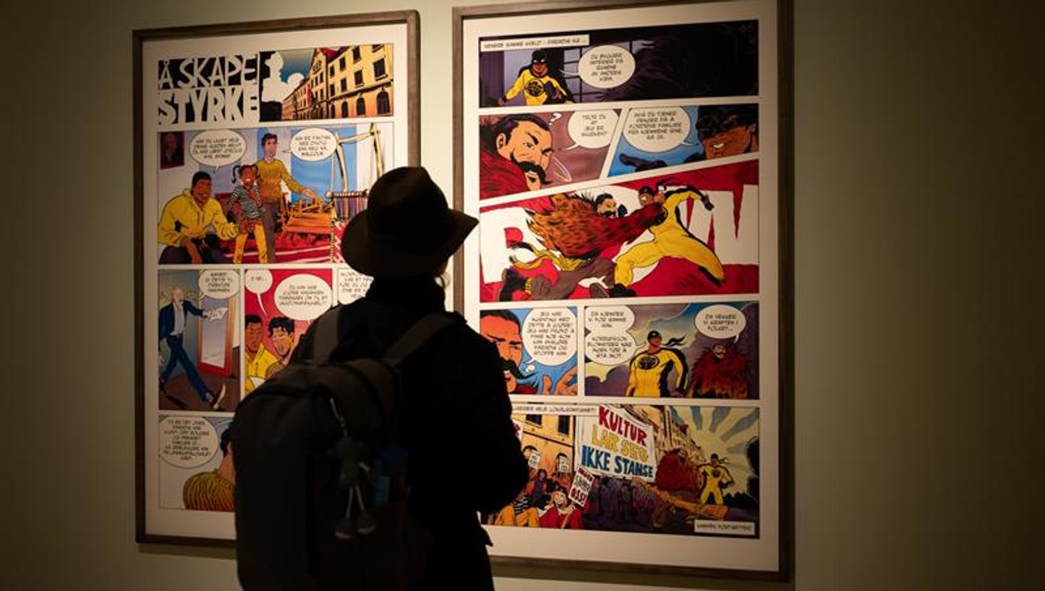 Visitor viewing framed comic book pages in a museum exhibition with subdued lighting.