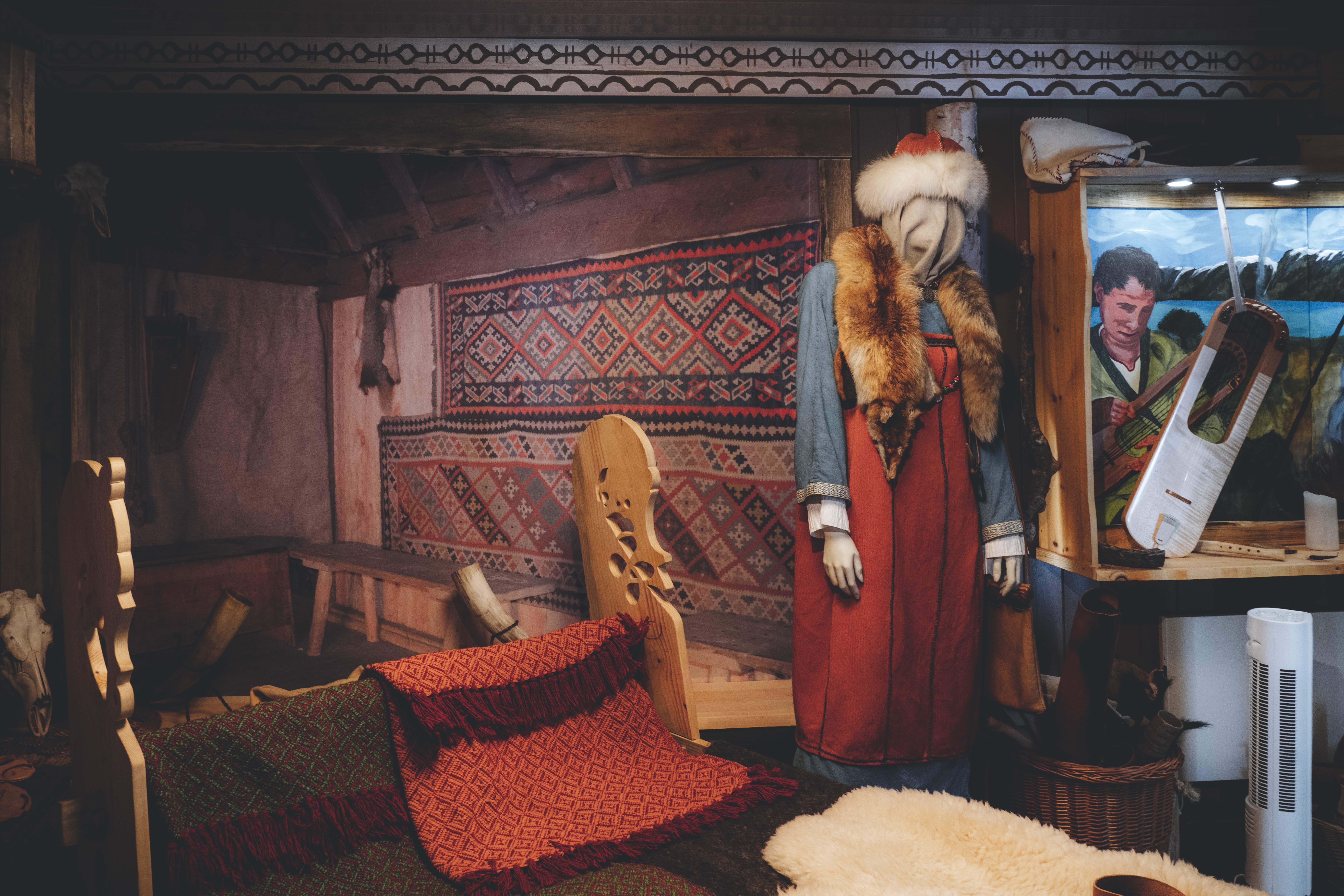 In der Wikingerausstellung hängen gewebte Teppiche an der Wand, eine Schaufensterpuppe in Wikingerkleidung und Hut.