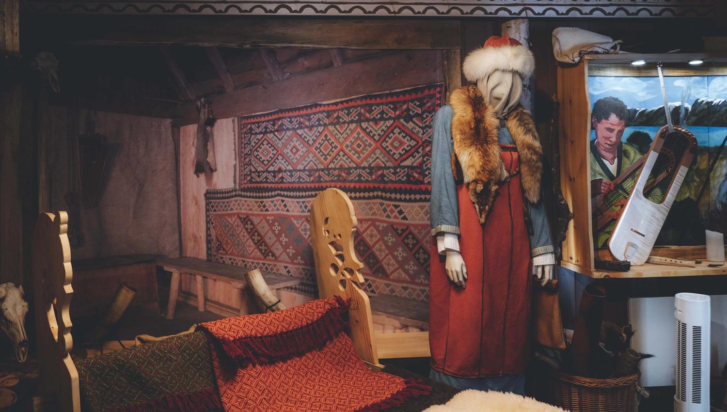 In der Wikingerausstellung hängen gewebte Teppiche an der Wand, eine Schaufensterpuppe in Wikingerkleidung und Hut.