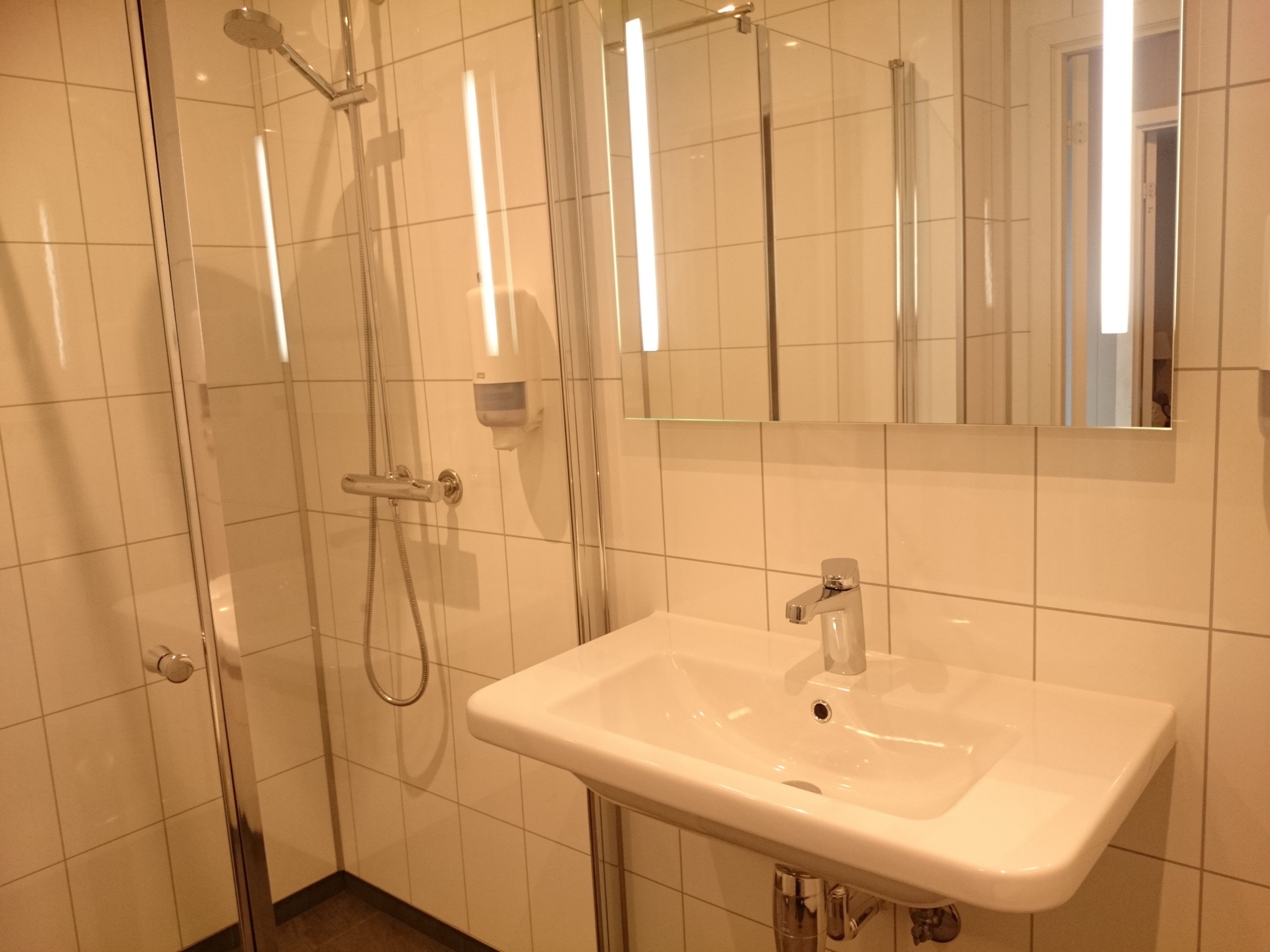 Clean and modern bathroom with shower, tiled walls and bright lighting at Ullensvang Gjesteheim.