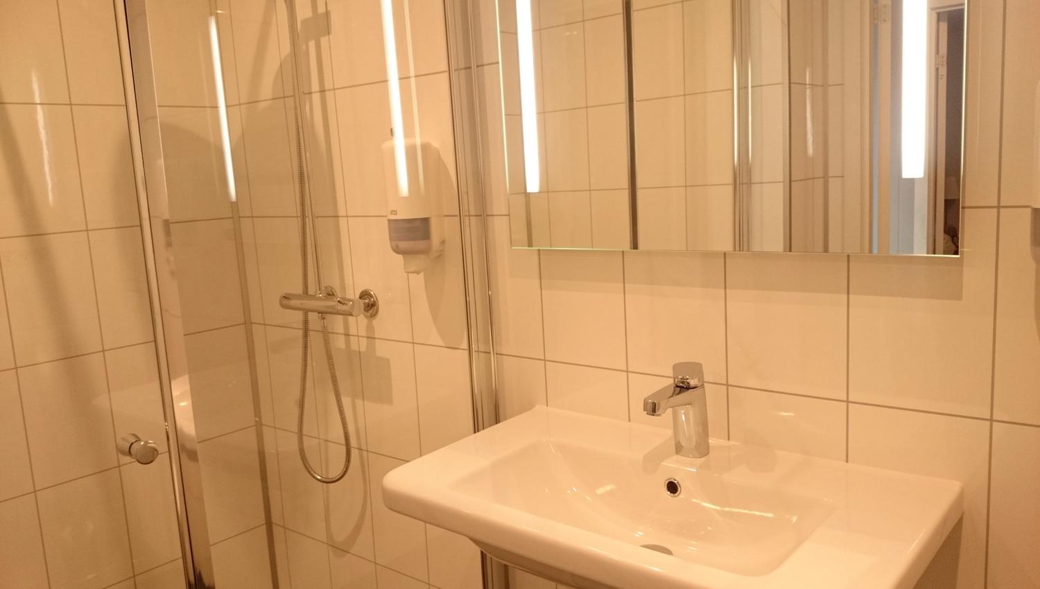 Clean and modern bathroom with shower, tiled walls and bright lighting at Ullensvang Gjesteheim.
