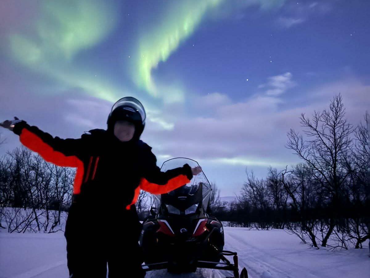 Guest beside a snowmobile under the Northern Lights