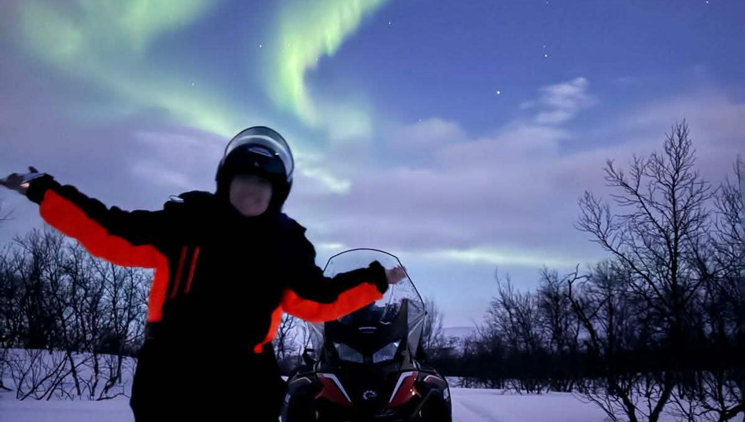 Guest beside a snowmobile under the Northern Lights