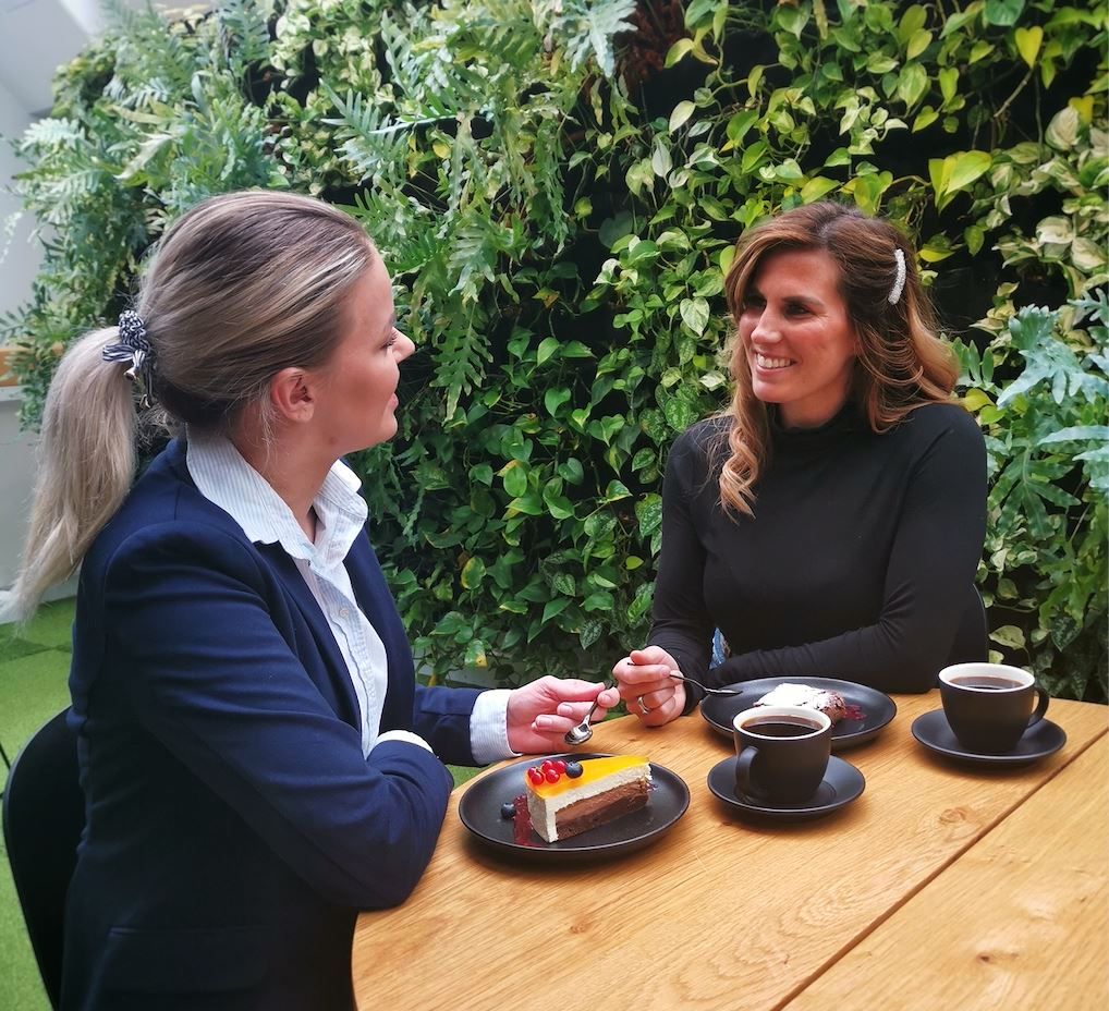 To personer med kaffe og kake ved et bord foran grønn bakgrunn