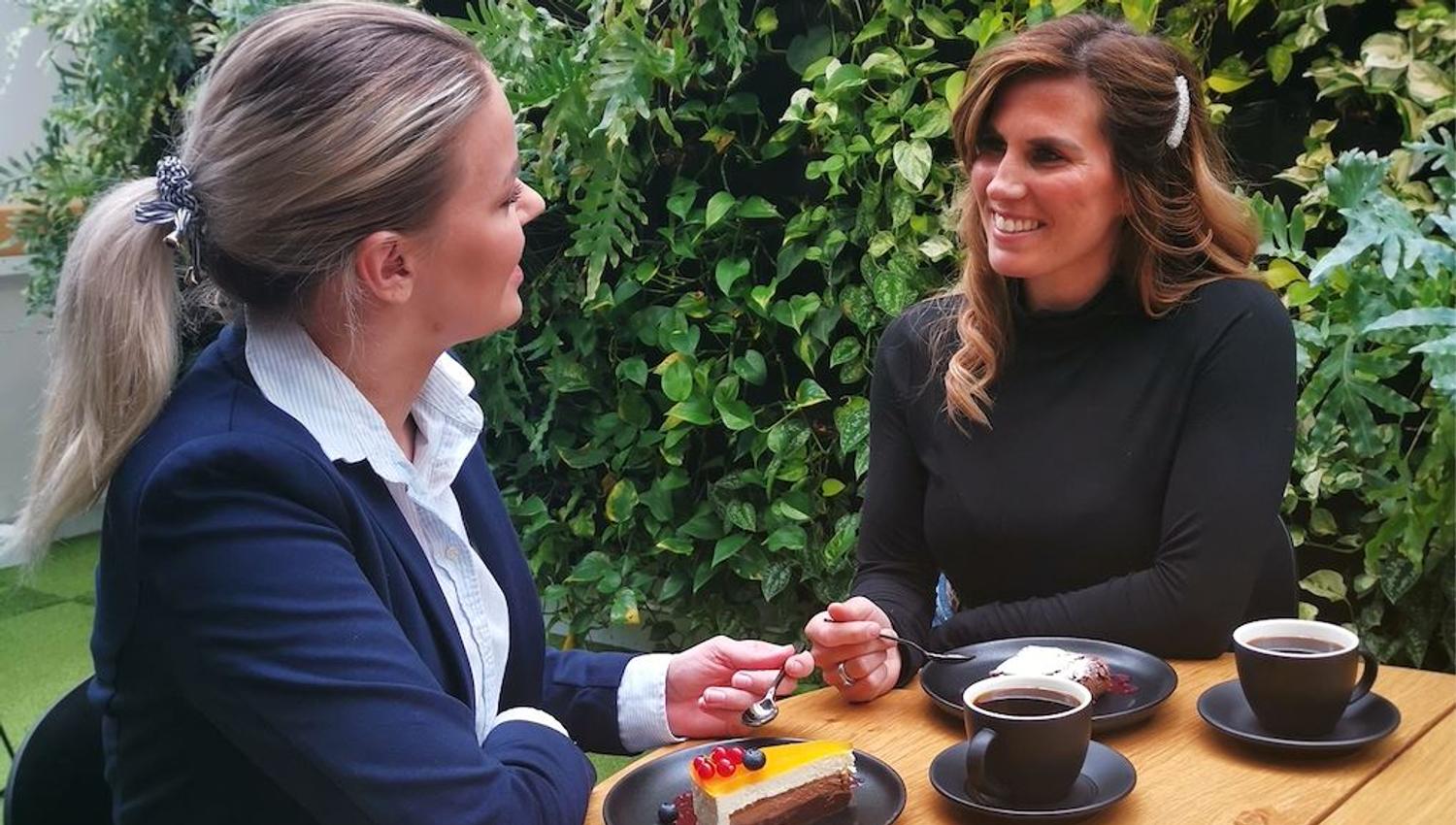 To personer med kaffe og kake ved et bord foran grønn bakgrunn