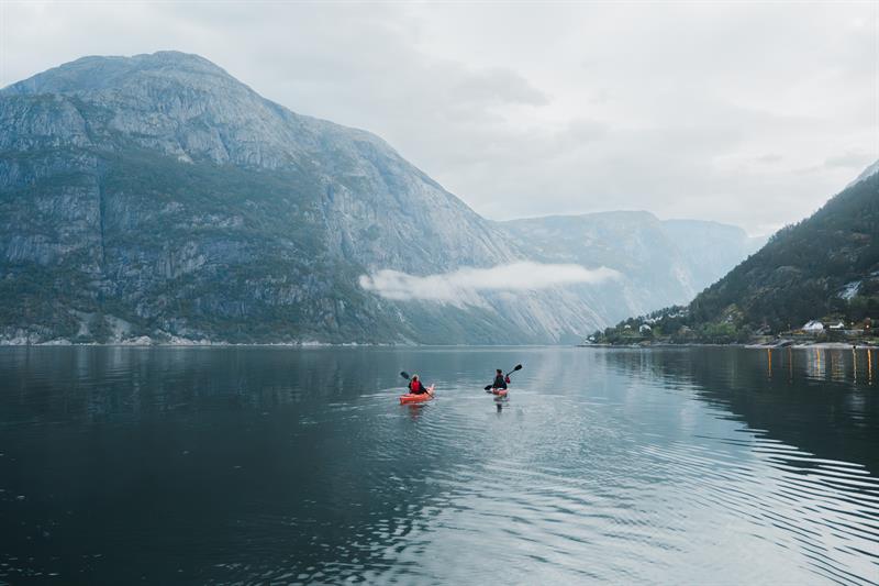 Et par padler kajakk på fjorden mot et stort fjell.