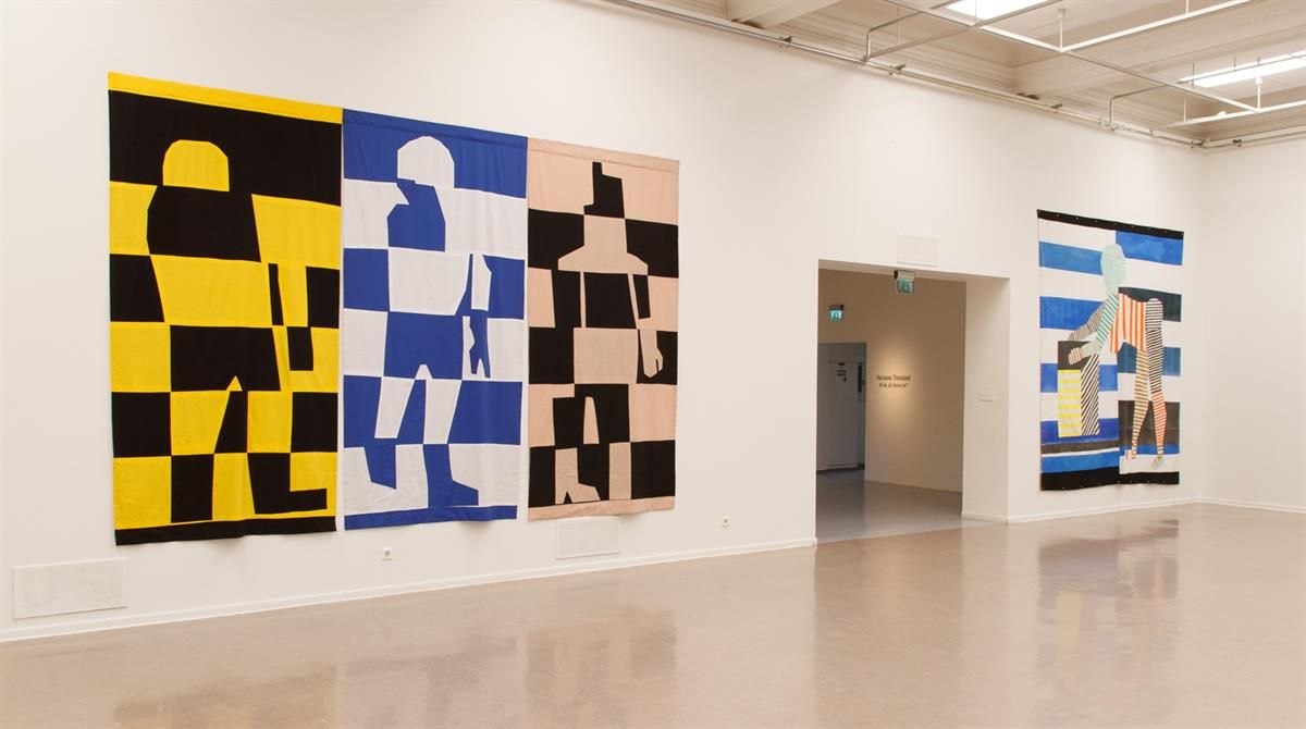 Large geometric paintings in yellow, blue, and black displayed in a bright gallery space.