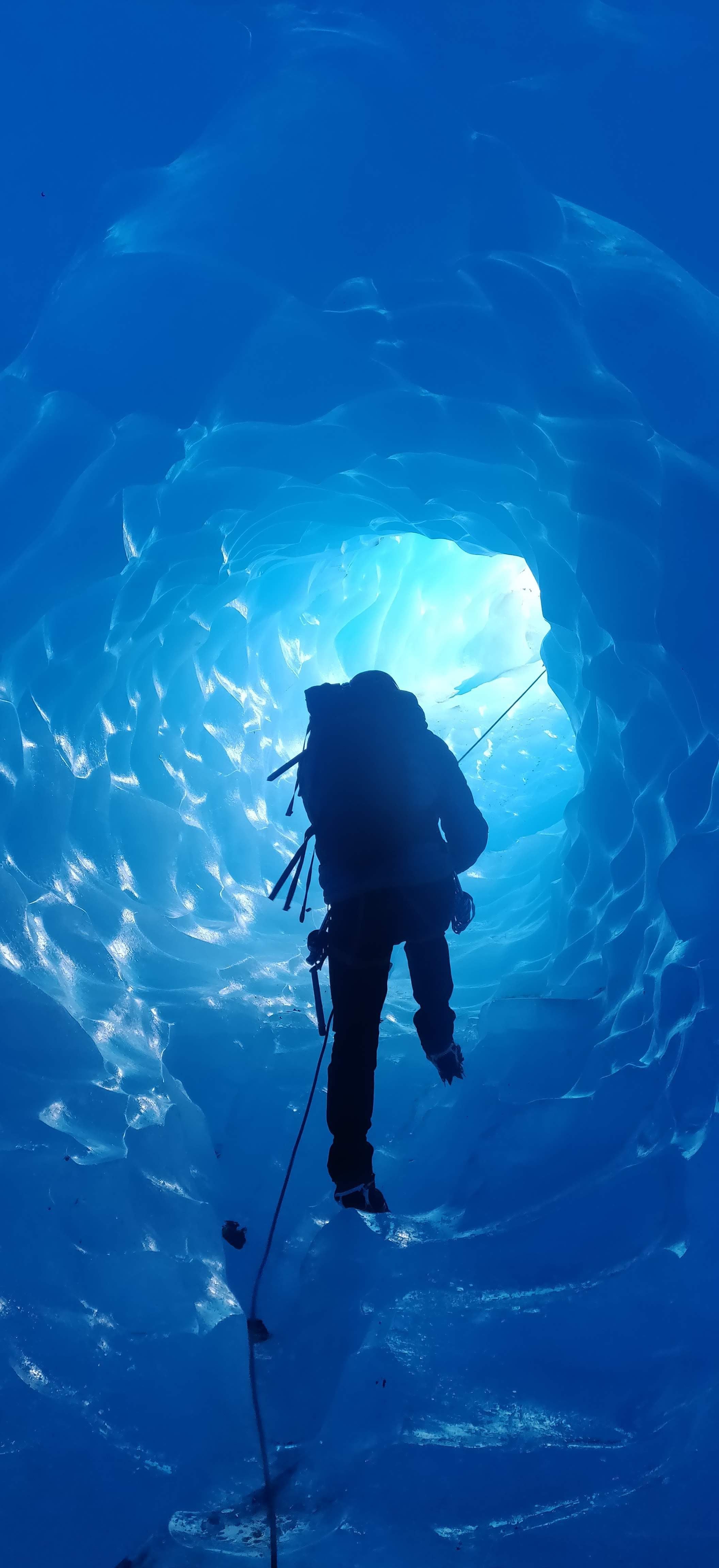 One person climbing inside a glacier, surrounded by blue ice.