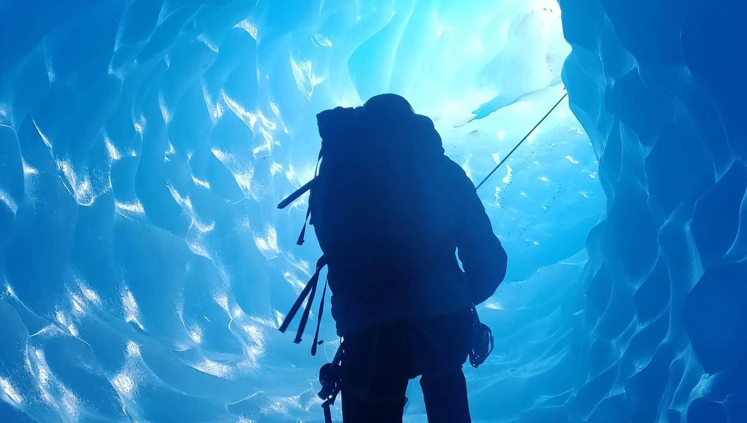 One person climbing inside a glacier, surrounded by blue ice.