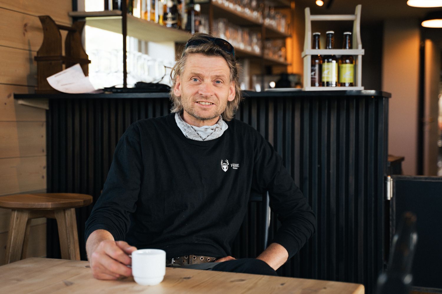 The owner at Halne mountain lodge, sitting at a table holding a cup of coffee.