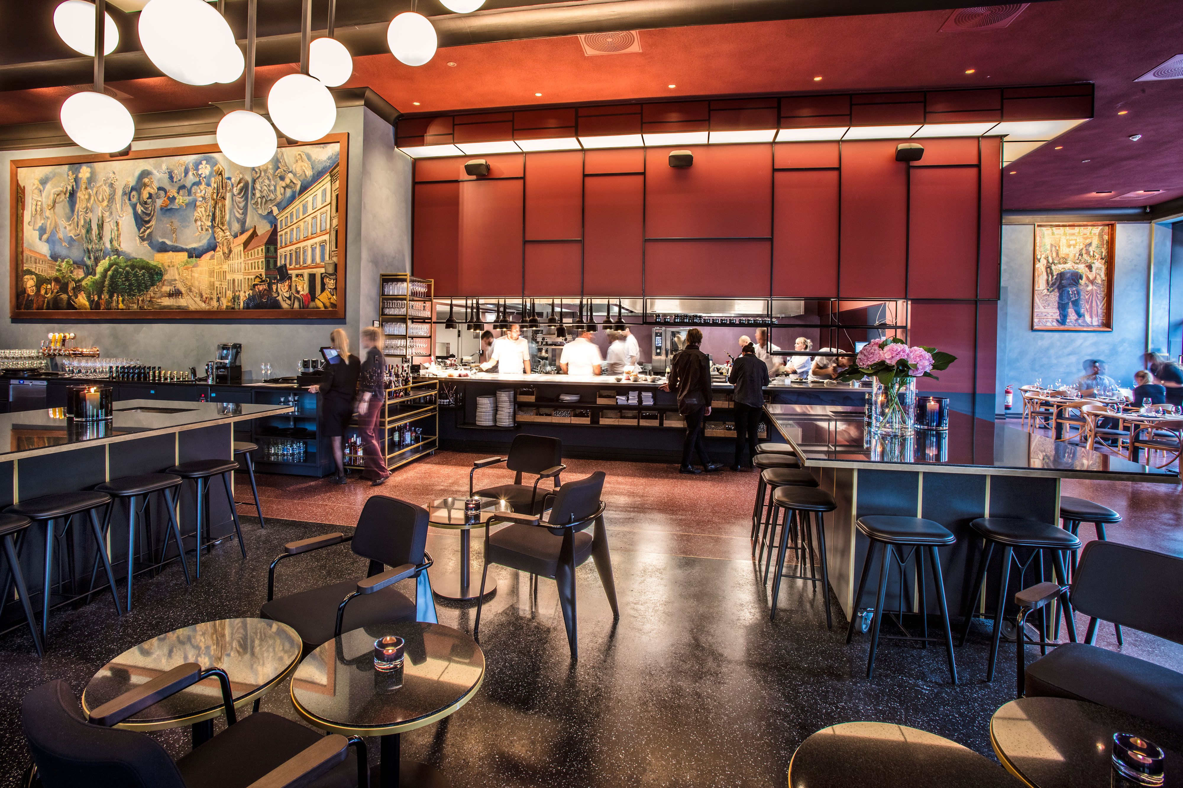 Interior with tables and chairs, bar tables and bar stools, and an open kitchen.