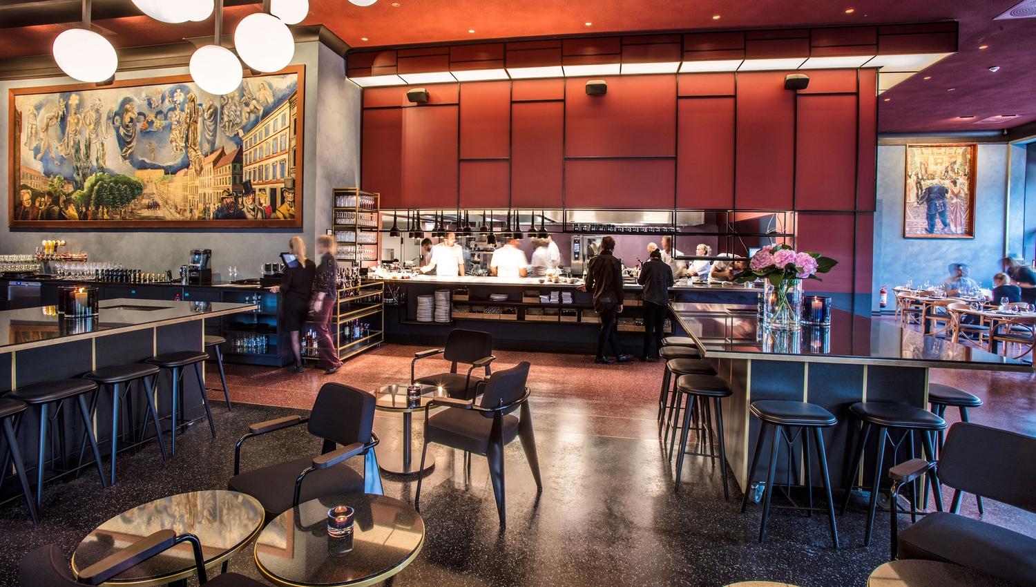 Interior with tables and chairs, bar tables and bar stools, and an open kitchen.