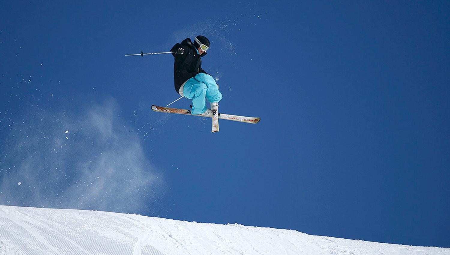 A skier jumps and crosses his skies. Blue skies in the backgound.