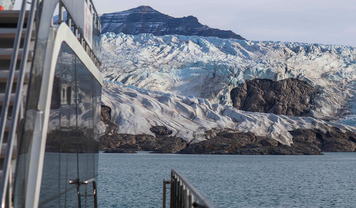A boat in the foreground with a fjord, glacier and a mountain in the background