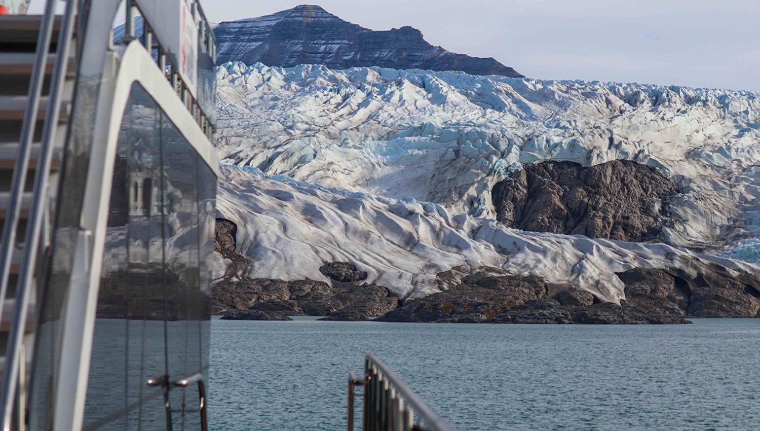 A boat in the foreground with a fjord, glacier and a mountain in the background