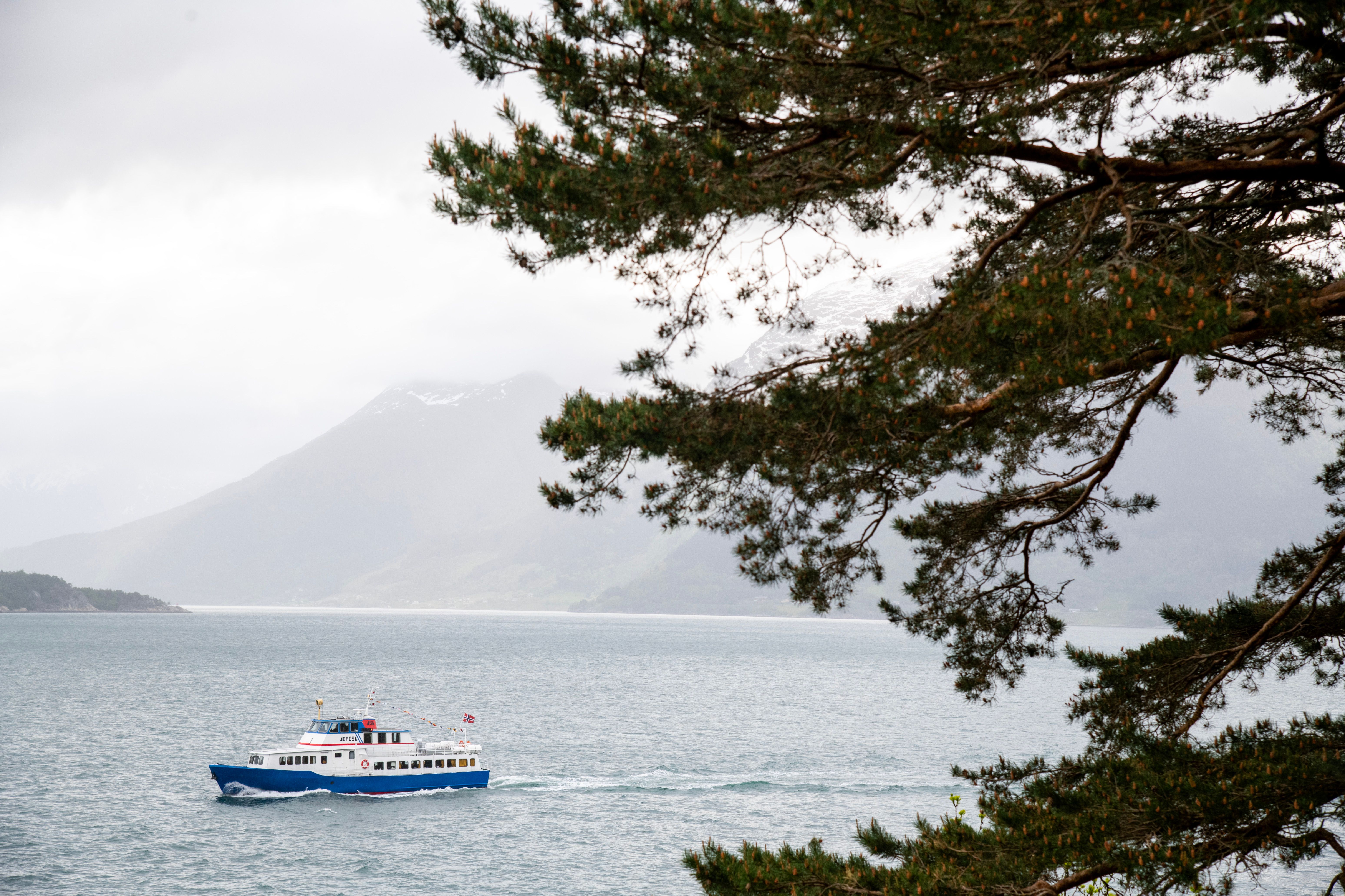 The literature boat Epos sailing through the Hardangerfjord, seen from shore with mountains in the background.