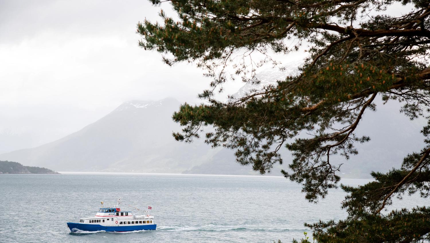 The literature boat Epos sailing through the Hardangerfjord, seen from shore with mountains in the background.