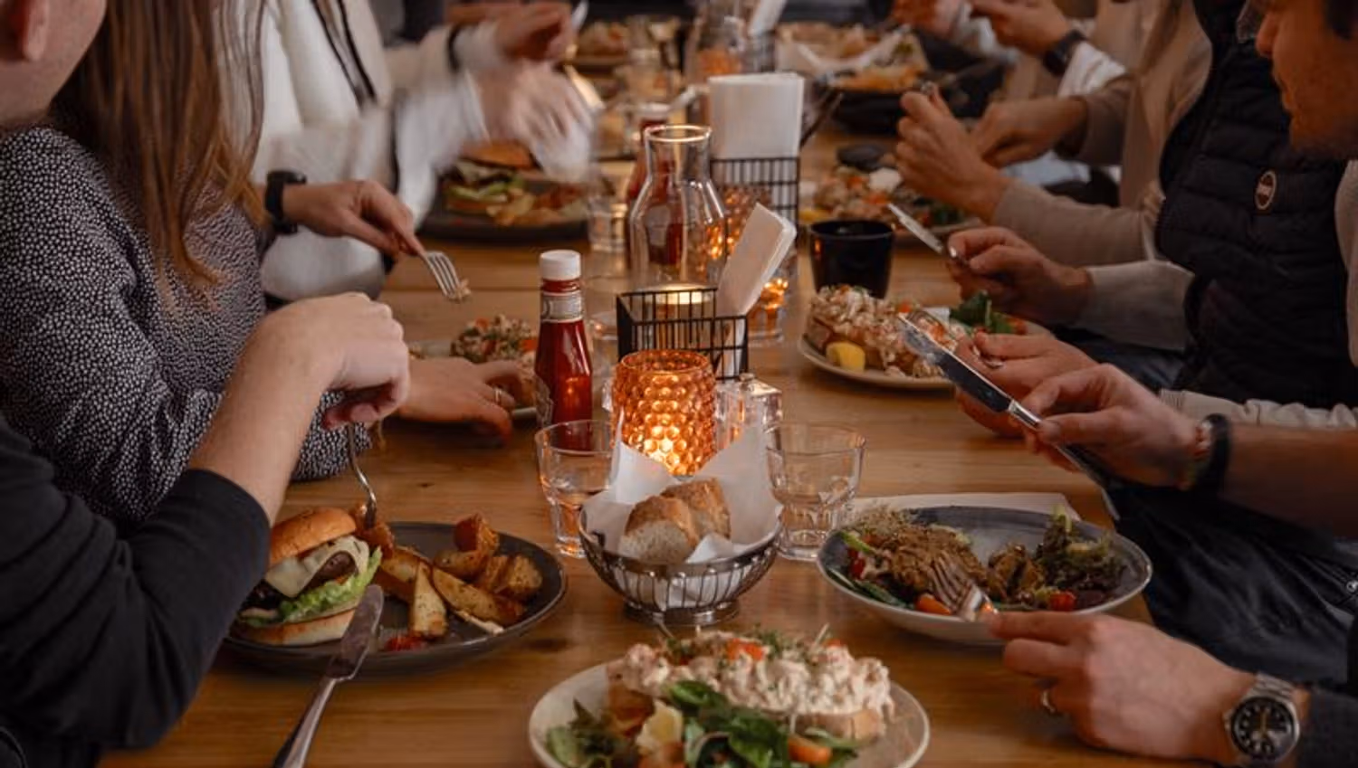 Gjester samlet rundt et langbord mens de nyter mat og drikke i en varm og sosial restaurantatmosfære.