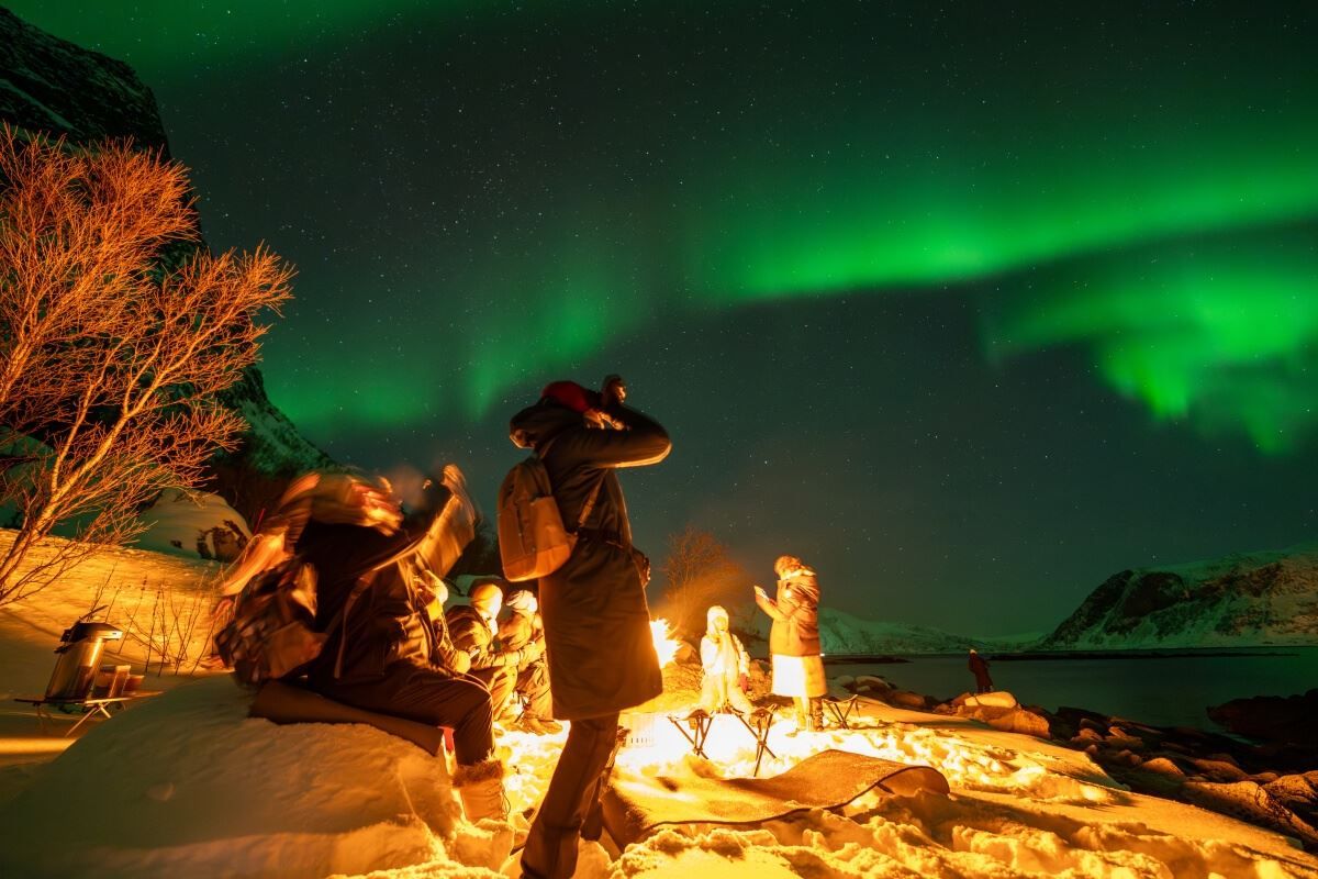 A guest photographs the Northern Lights from beside the campfire.