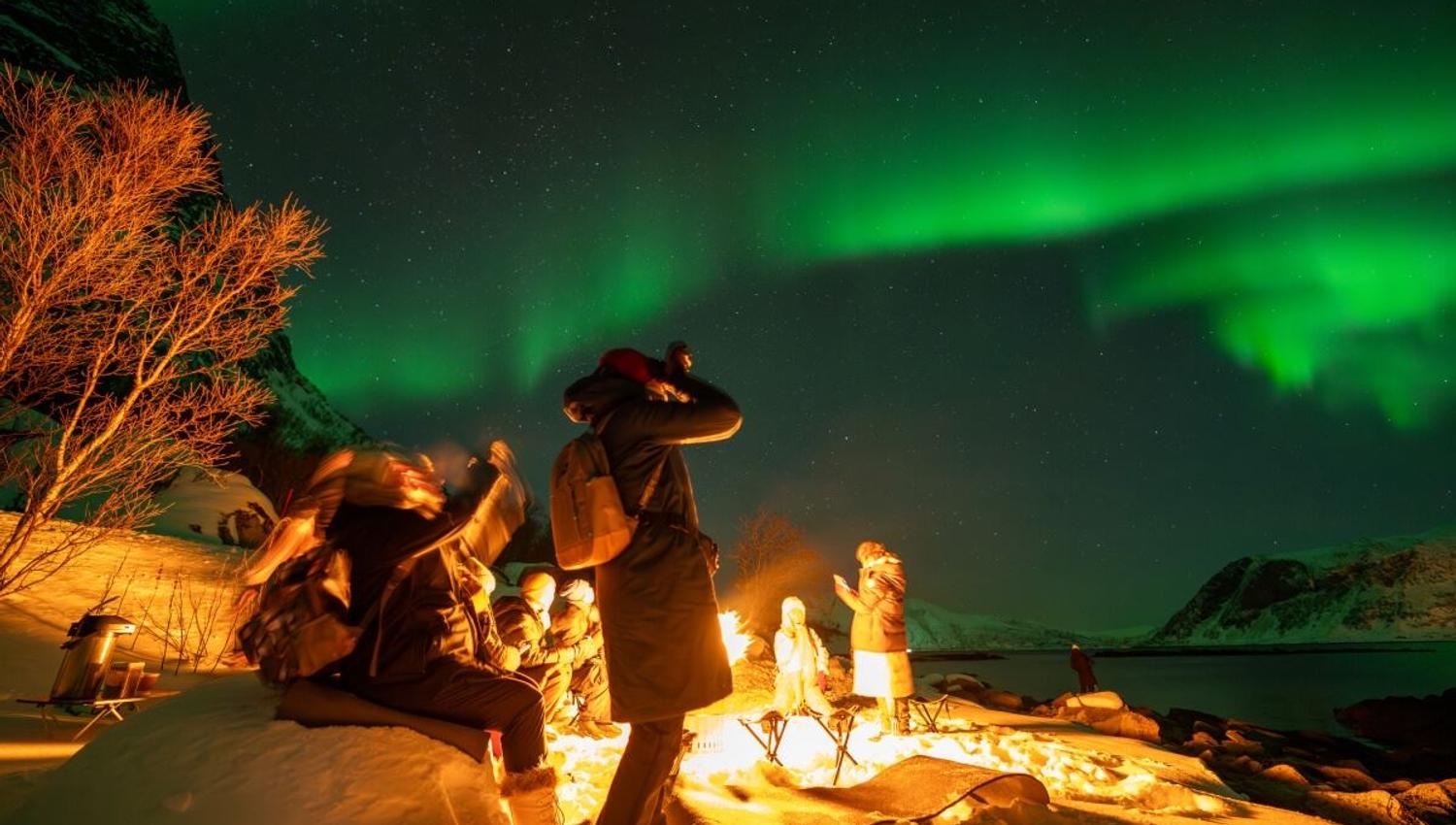A guest photographs the Northern Lights from beside the campfire.