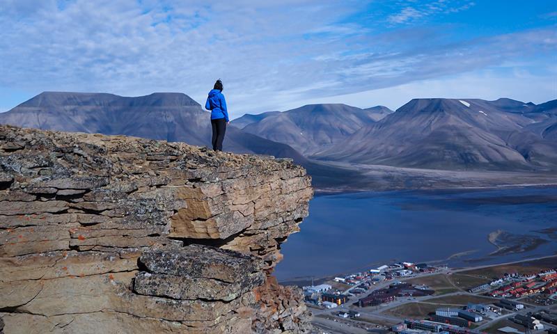 Person står på fjelltopp og ser på utsikten over longyearbyen