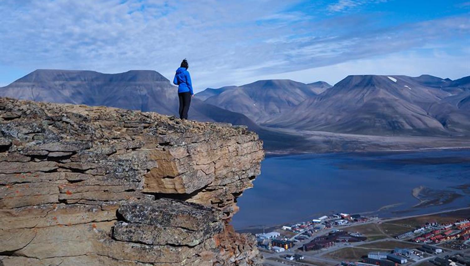 Person står på fjelltopp og ser på utsikten over longyearbyen