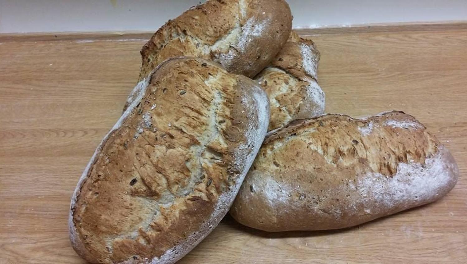 Several flour-dusted rustic bread loaves stacked on a wooden table, with a plain wall in the background.