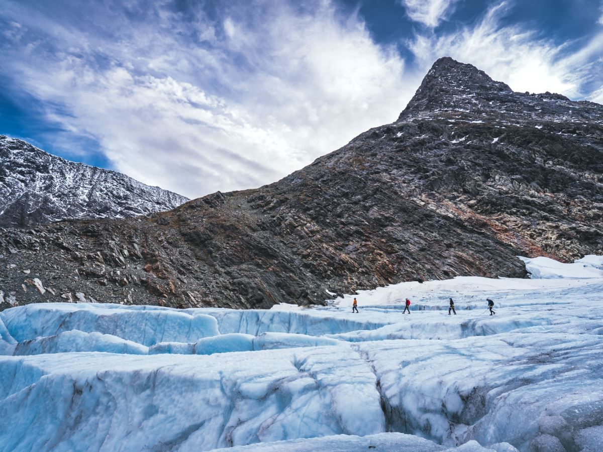 Four persons walking on a glacier.