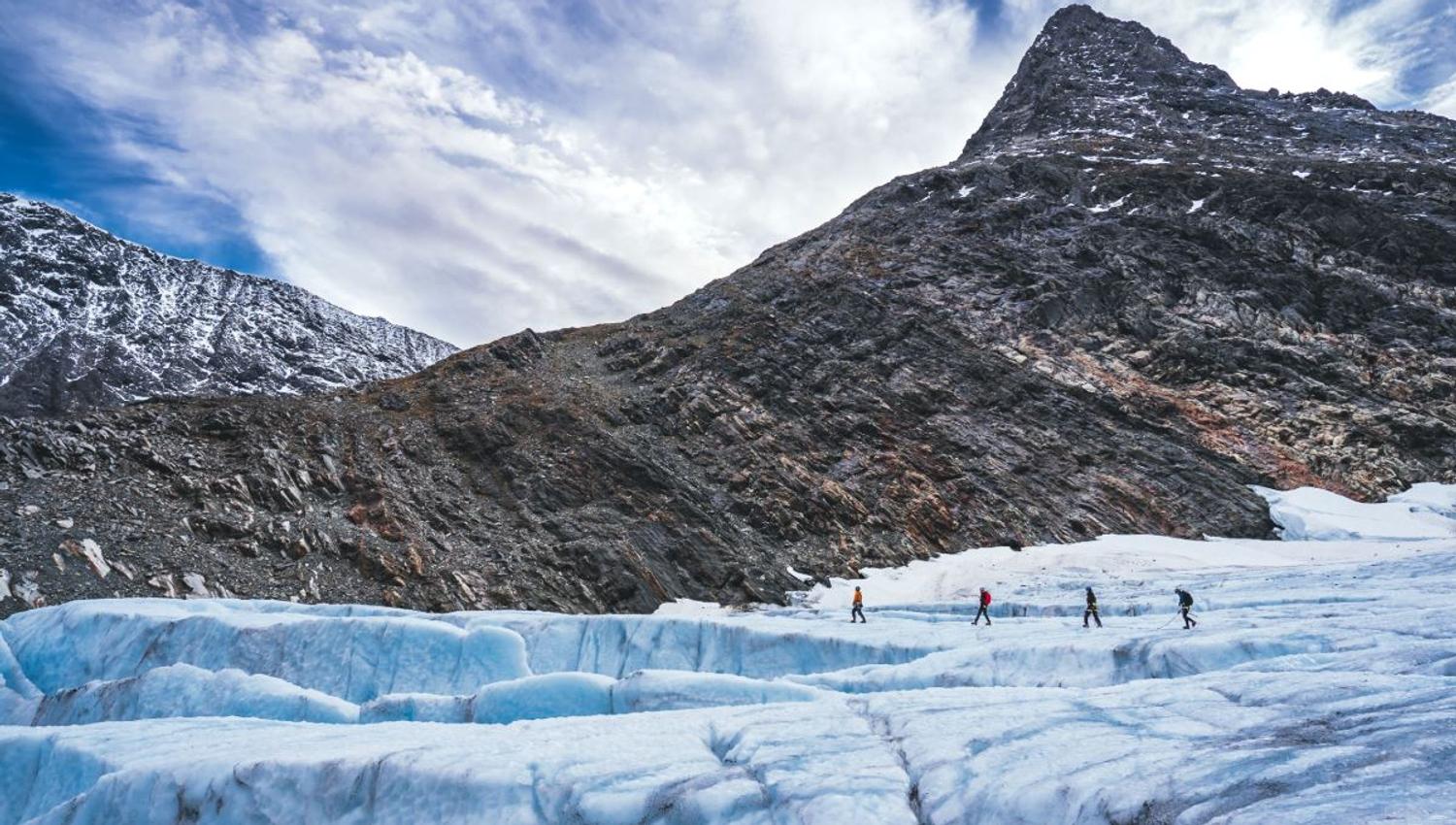 Four persons walking on a glacier.