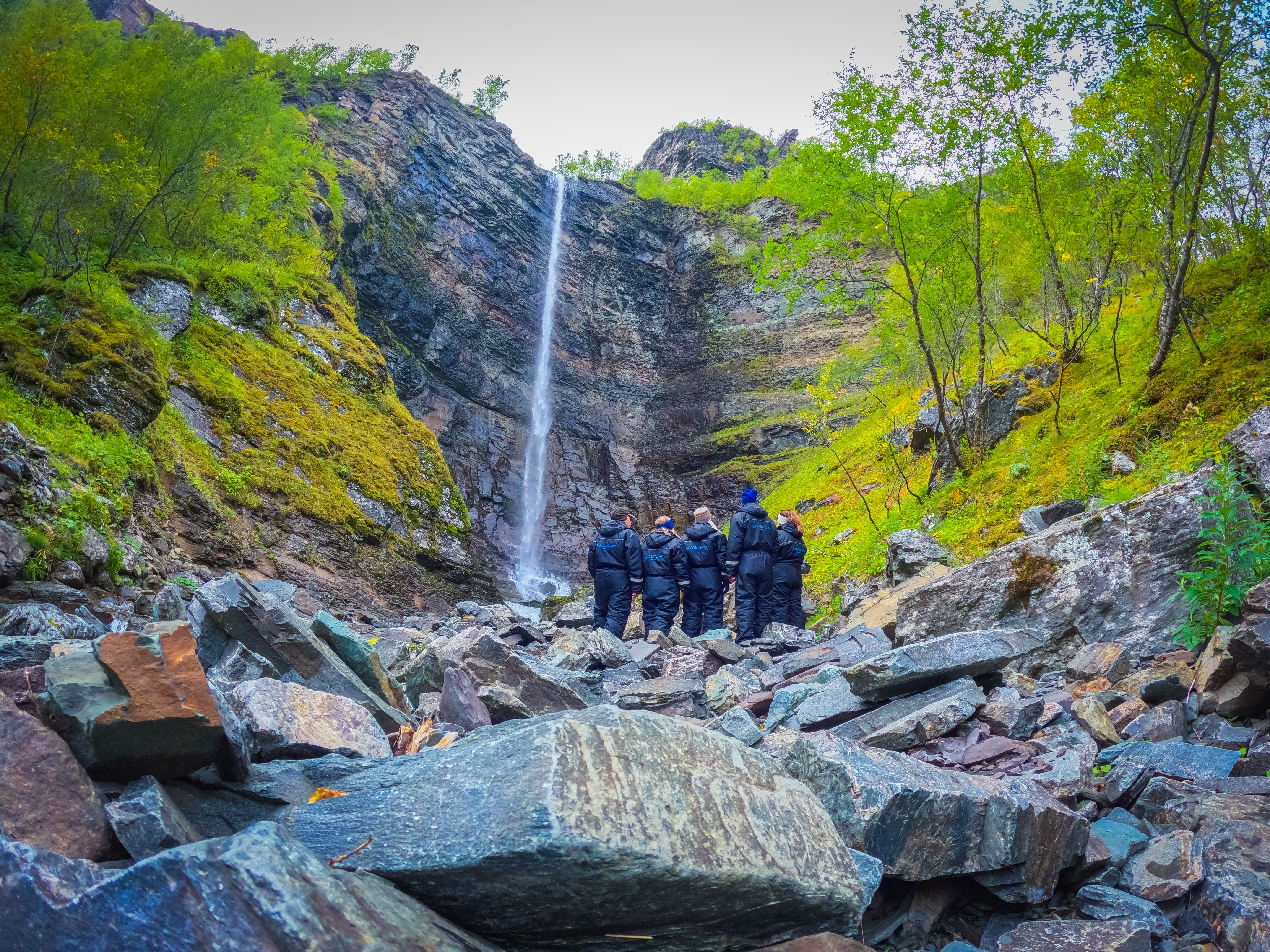 Groupe de personnes admirant une cascade dans un paysage rocheux verdoyant.