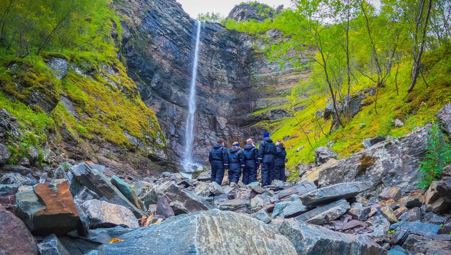 Groupe de personnes admirant une cascade dans un paysage rocheux verdoyant.