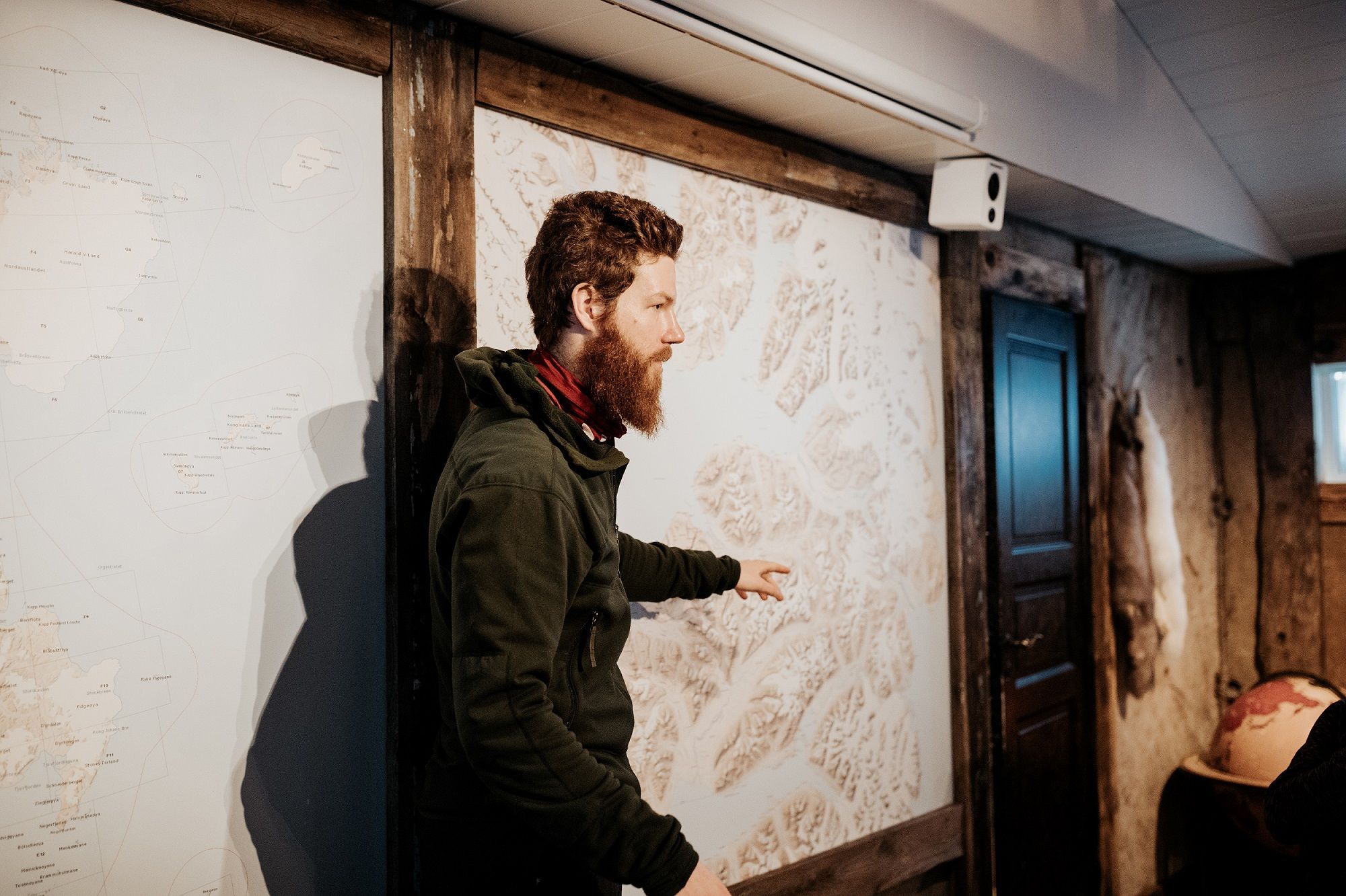 A guide pointing out a trip route on a map hanging on a wall in the background