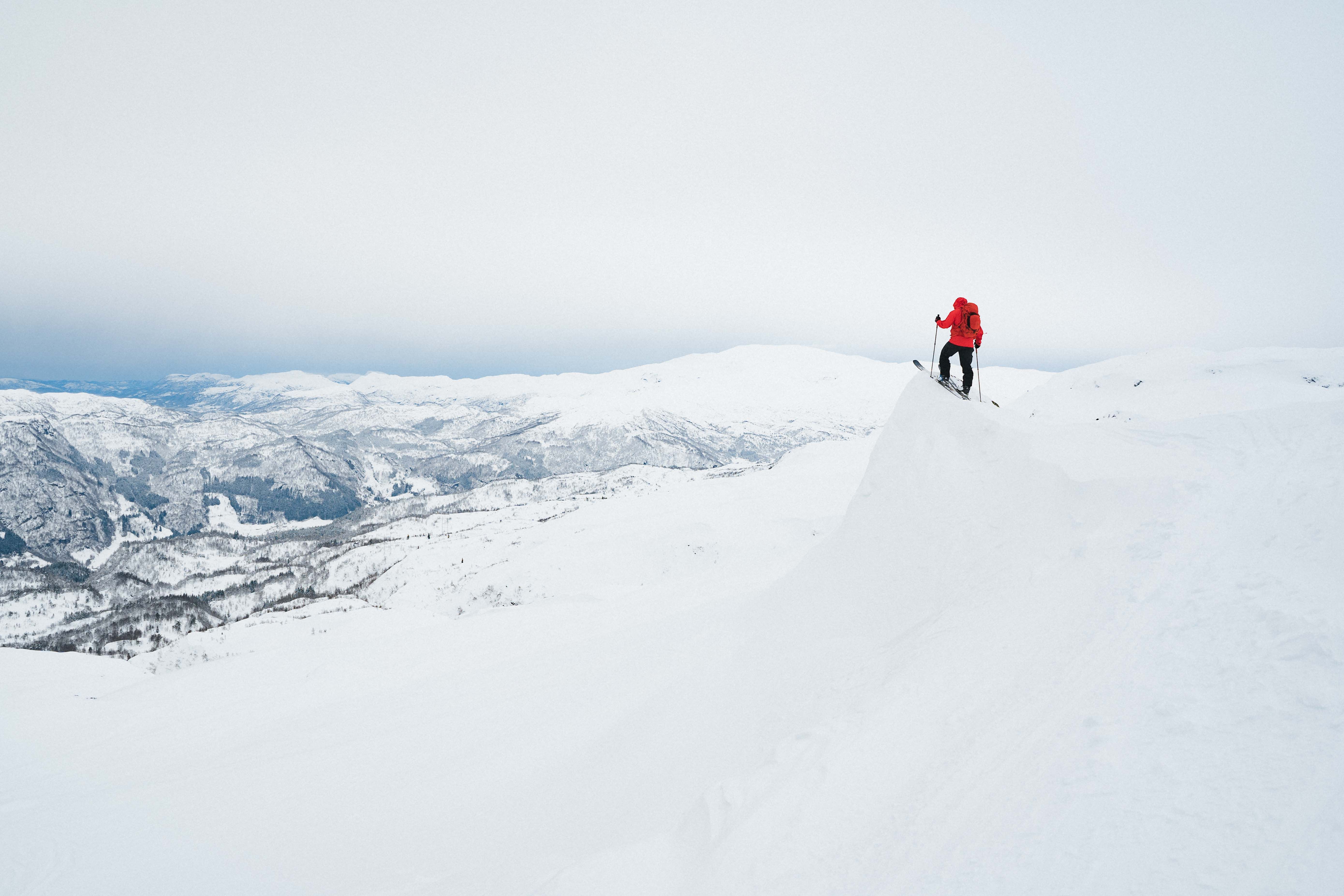 A person on skiis standing on a cliff and looking out over a snow-covered landscape.  
